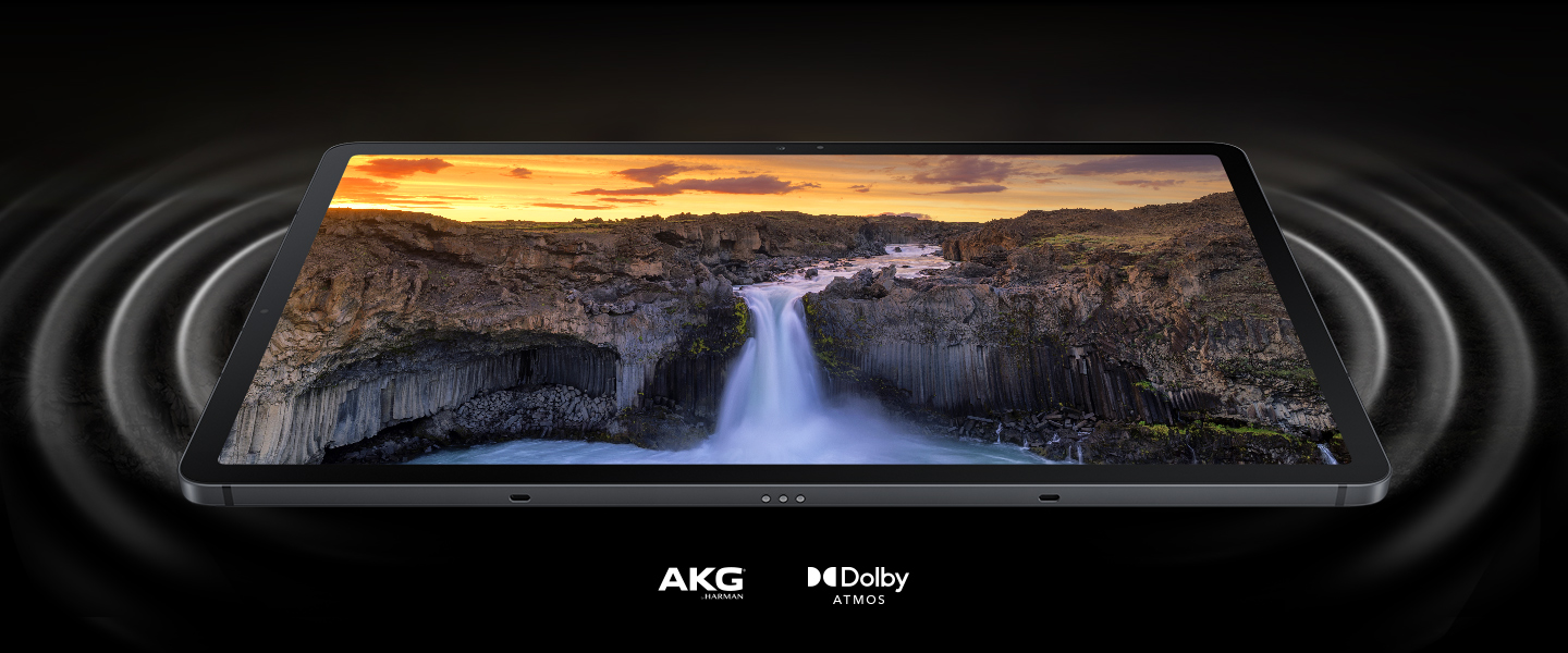 Galaxy Tab S7 FE 5G syns på rygg med en levande scen i landskapet på skärmen. På vardera sidan av surfplattan finns cirklar som representerar ljudvågor som kommer ut från de dubbla högtalarna och visar hur djupt ljudet är. AKG-logotyp och Dolby Atmos-logotyp.
                                                                