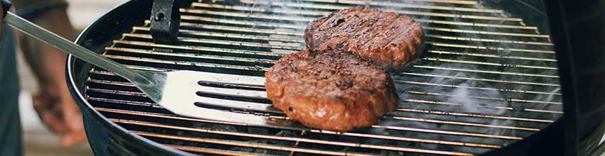 Två grillbiffar vänds med stekspade på en klotgrill med rök och värme.