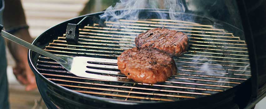 Grillbiffar steks över glödande kol på en klassisk kolgrill med grillredskap i användning.