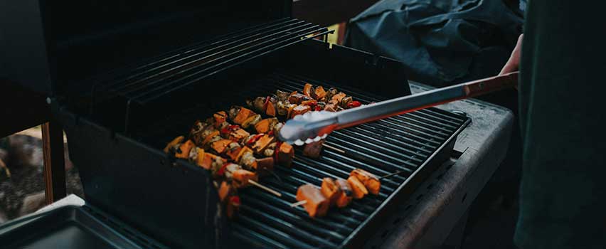 Grillspett tillagas på gasolgrill på terrassen i dämpat kvällsljus med en person som lagar mat.