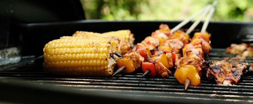 Grillade majskolvar och kycklingspett med paprika på grillgaller, perfekt för sommarmat och utomhusgrillupplevelser.