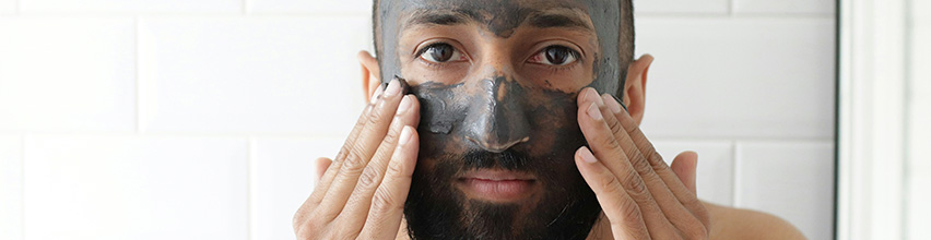 En man smörjer in en grå ansiktsmask i ansiktet med båda händerna.