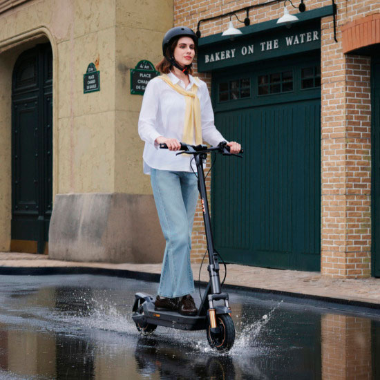 Kvinna med hjälm kör Navee GT elsparkcykel genom vattenpöl på kullerstensgata – stänkskyddad och stadsanpassad