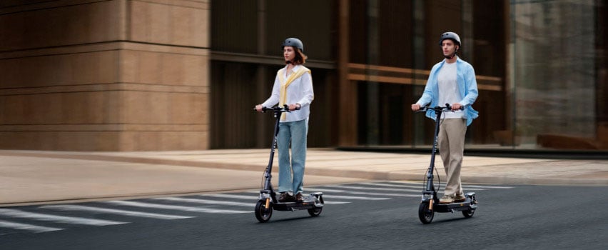 Två personer kör Navee GT5 Max elsparkcyklar sida vid sida i staden – perfekt för daglig pendling