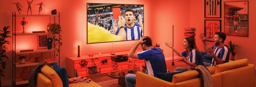 Vänner jublar över fotbollsmål på TV med intensiv blå WiZ Sports Live-belysning i vardagsrummet