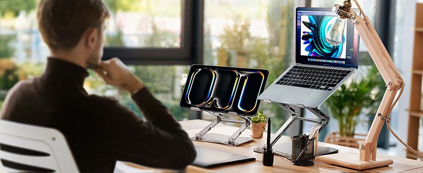 Man arbetar vid skrivbord med laptop och surfplatta på Wozinsky justerbart ställ i ljust kontor vid fönster