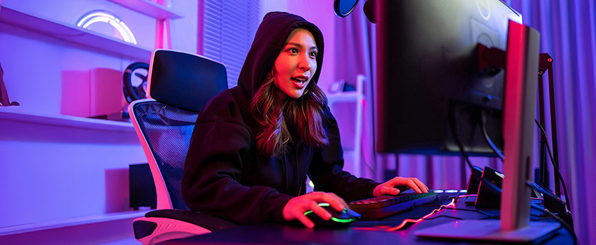 Ung kvinna spelar vid datorn med Wozinsky gaming-mus och tangentbord i mörkt rum med lila RGB-belysning