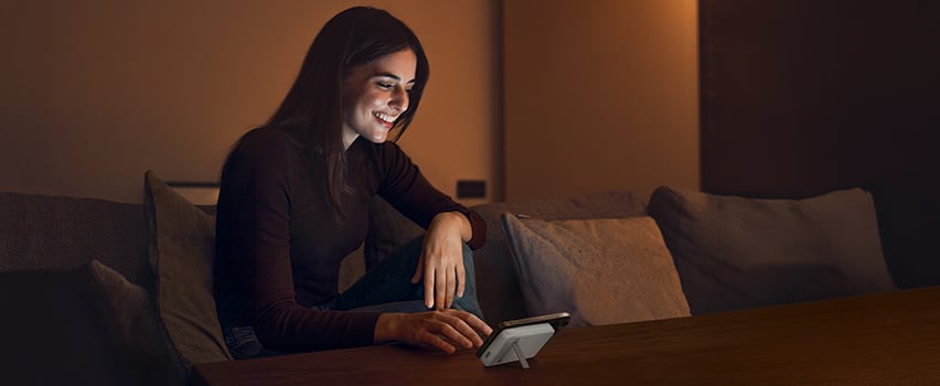 Kvinna ler medan hon trådlöst laddar sin smartphone med Wozinsky powerbank på bord i mysigt kvällsljus