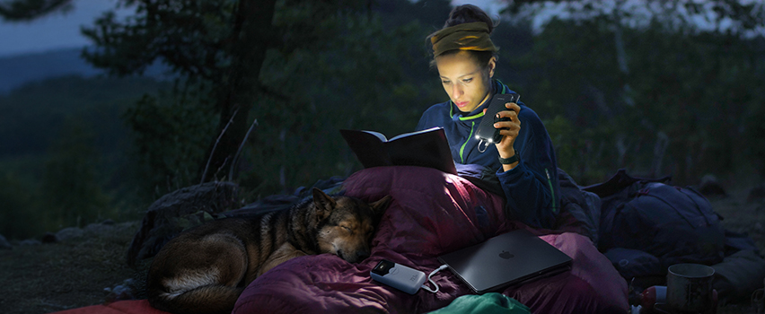 Kvinna läser bok i tält med hund och laddar smartphone och laptop med Wozinsky powerbank och pannlampa