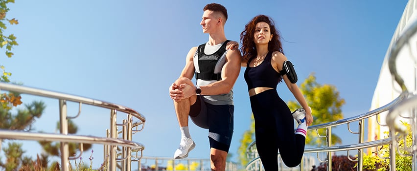 Par tränar utomhus i sportkläder med Wozinsky viktvest och löpararmband för smartphone på solig dag